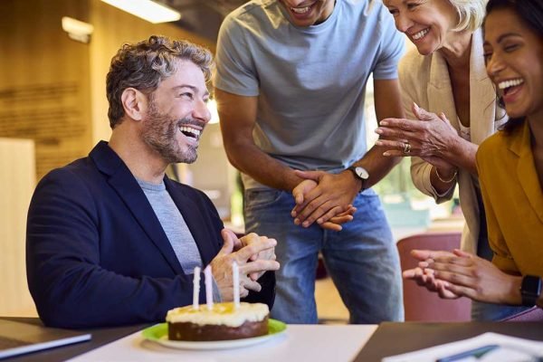 Staff Celebrating Birthday Of Male Colleague At Desk In Office W
